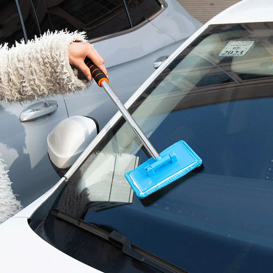 Person cleaning a car window with a blue squeegee and orange handle.